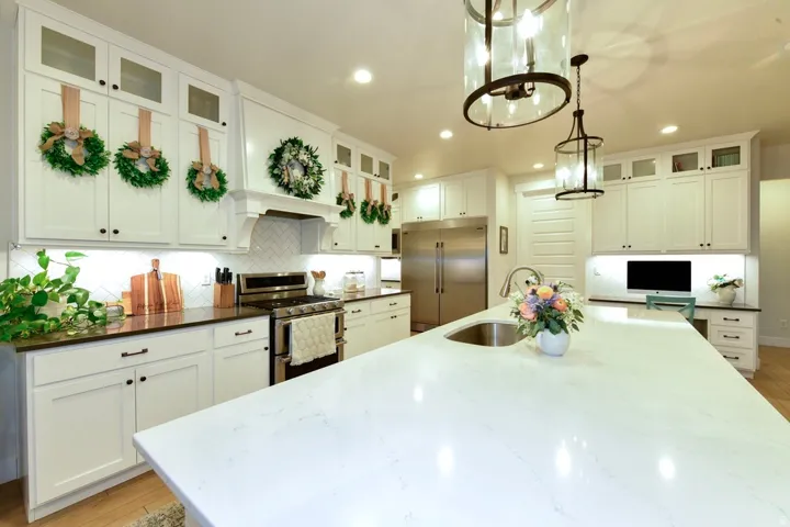 Kitchen featuring a large central island with an undermount sink, white shaker cabinetry, stainless steel appliances, dark countertops, and a white herringbone tile backsplash