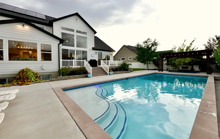 Spacious backyard featuring an in-ground swimming pool with integrated steps, extensive concrete decking, and a wood pergola