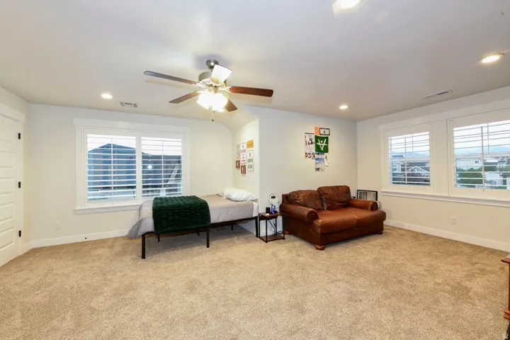 Carpeted room featuring multiple windows with louvered blinds, a ceiling fan with integrated lighting, and recessed ceiling lights