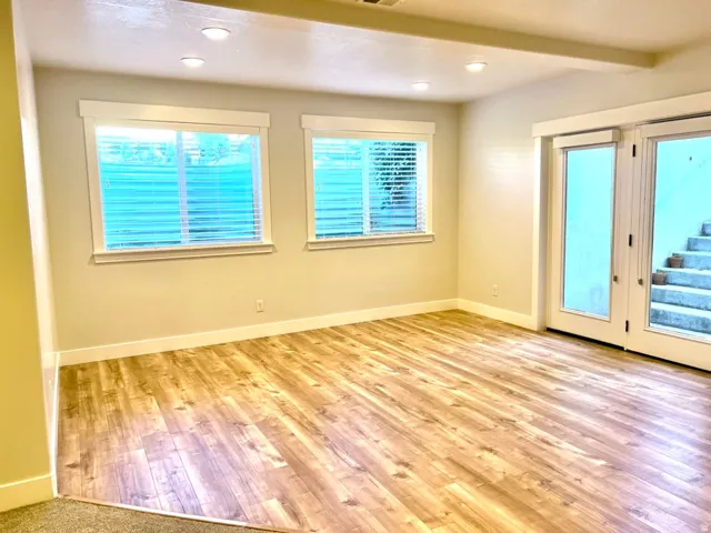 Spacious room featuring wood-finish flooring, two windows with blinds, recessed lighting, and a double glass-paneled door