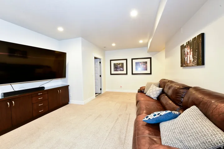 Recessed lighting illuminates a spacious room featuring wall-to-wall carpeting and a built-in media console with dark wood cabinetry and ample storage