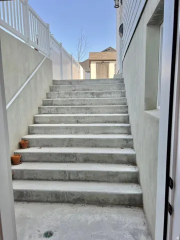 Exterior concrete staircase with an adjacent white vinyl fence and a small detached shed
