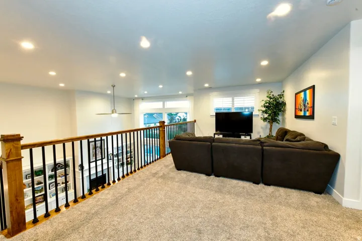 Carpeted loft area featuring a wood and metal railing, recessed lighting, and a ceiling fan
