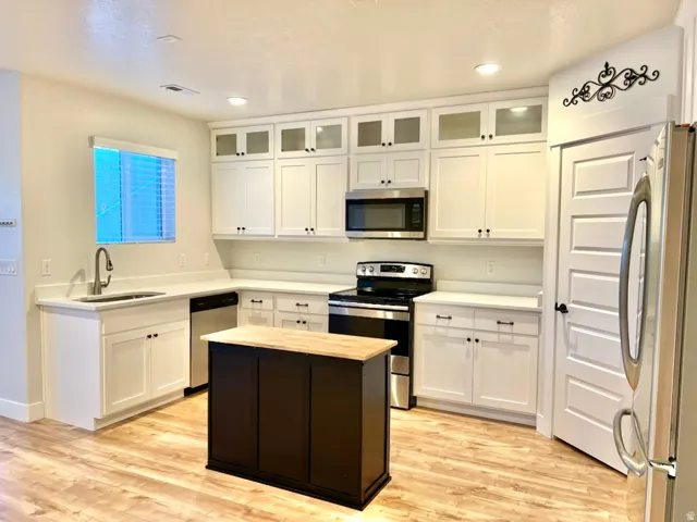 Bright kitchen featuring white cabinetry, stainless steel appliances, a center island with a wood-finish countertop, and wood-finish flooring