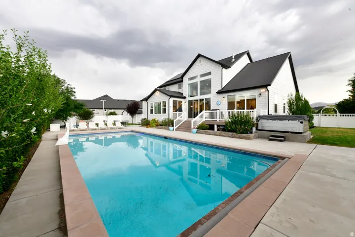 Spacious backyard featuring an in-ground swimming pool, concrete patio, and an integrated hot tub