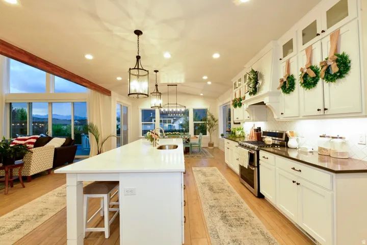 Open-concept kitchen and living area featuring white cabinetry, wood-finish flooring, a large kitchen island with integrated sink, stainless steel appliances, and a tiled backsplash
