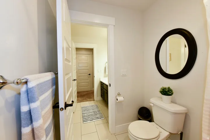 Bathroom featuring a white toilet, a circular mirror with a dark frame, and light-colored tile flooring