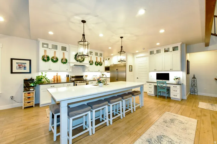 Spacious kitchen featuring an oversized island with seating, white shaker cabinetry, stainless steel appliances, and wood-finish flooring