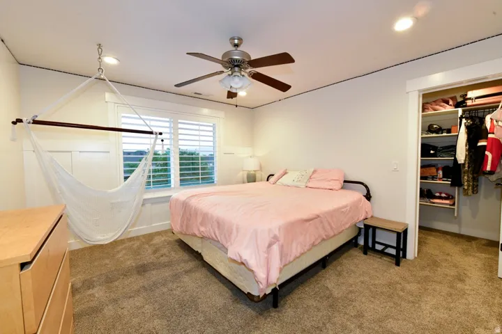 Carpeted room featuring a window with white plantation shutters, white wainscoting, and a ceiling fan with integrated lighting