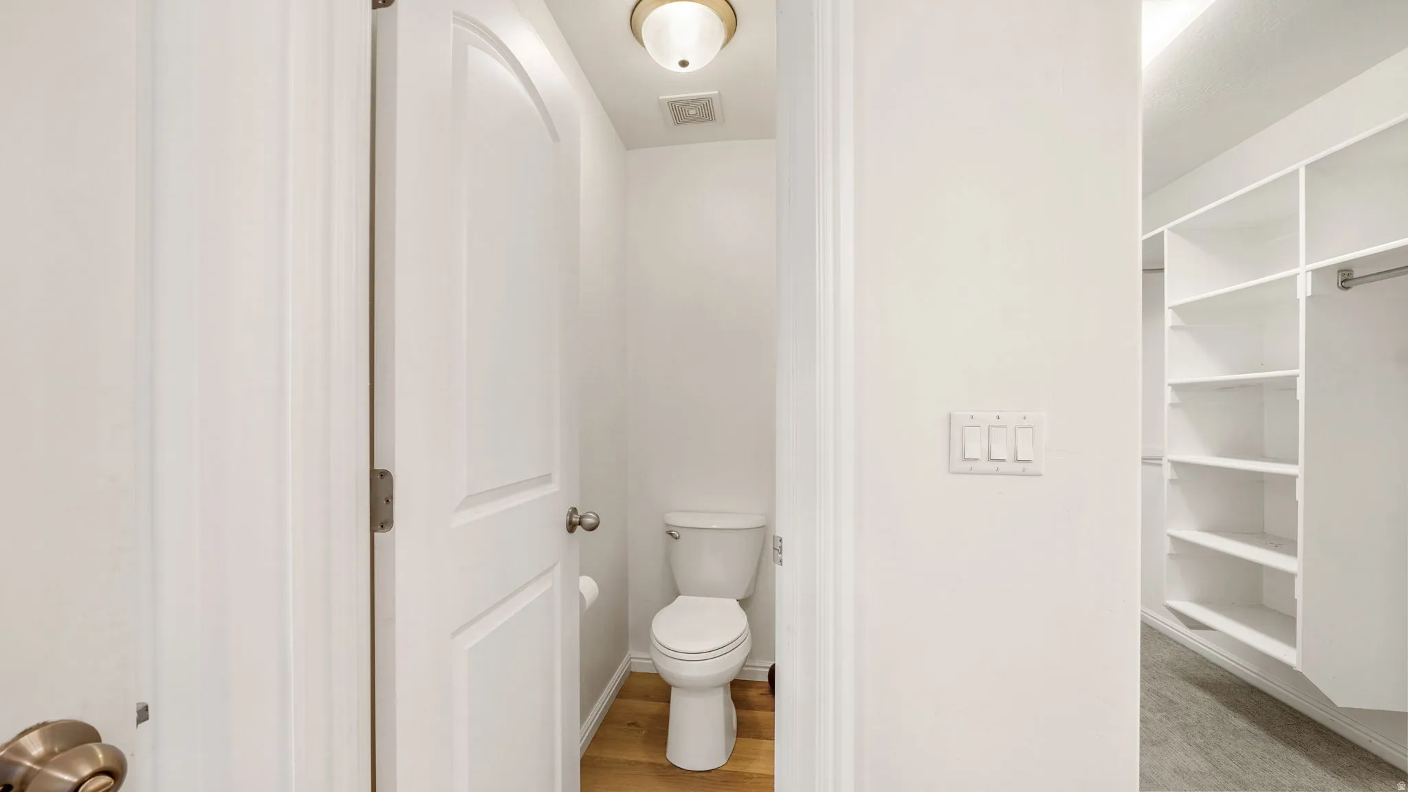 Hallway featuring a built-in closet system, a separate water closet with wood-finish flooring, and white walls