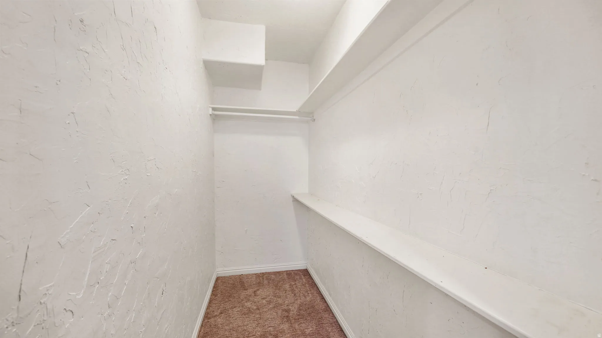 Integrated closet system featuring white shelving, hanging rod, and textured white walls