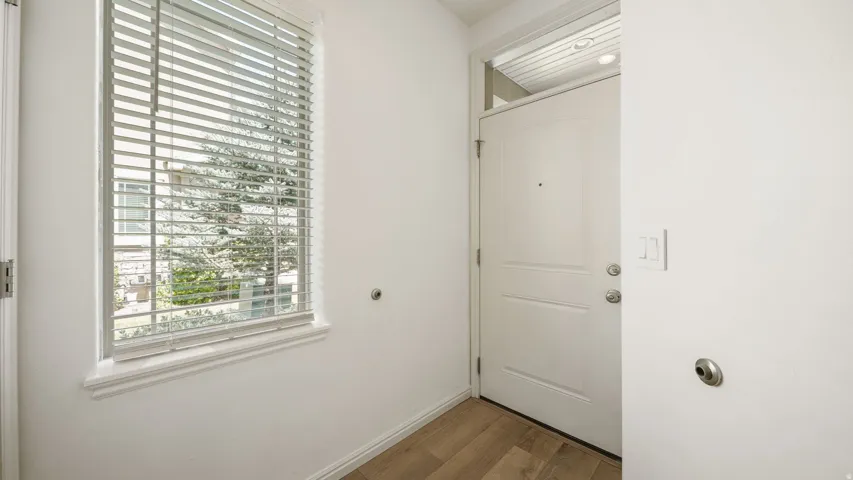 Entryway featuring a paneled door with a transom window, wood-finish flooring, and a window with horizontal blinds