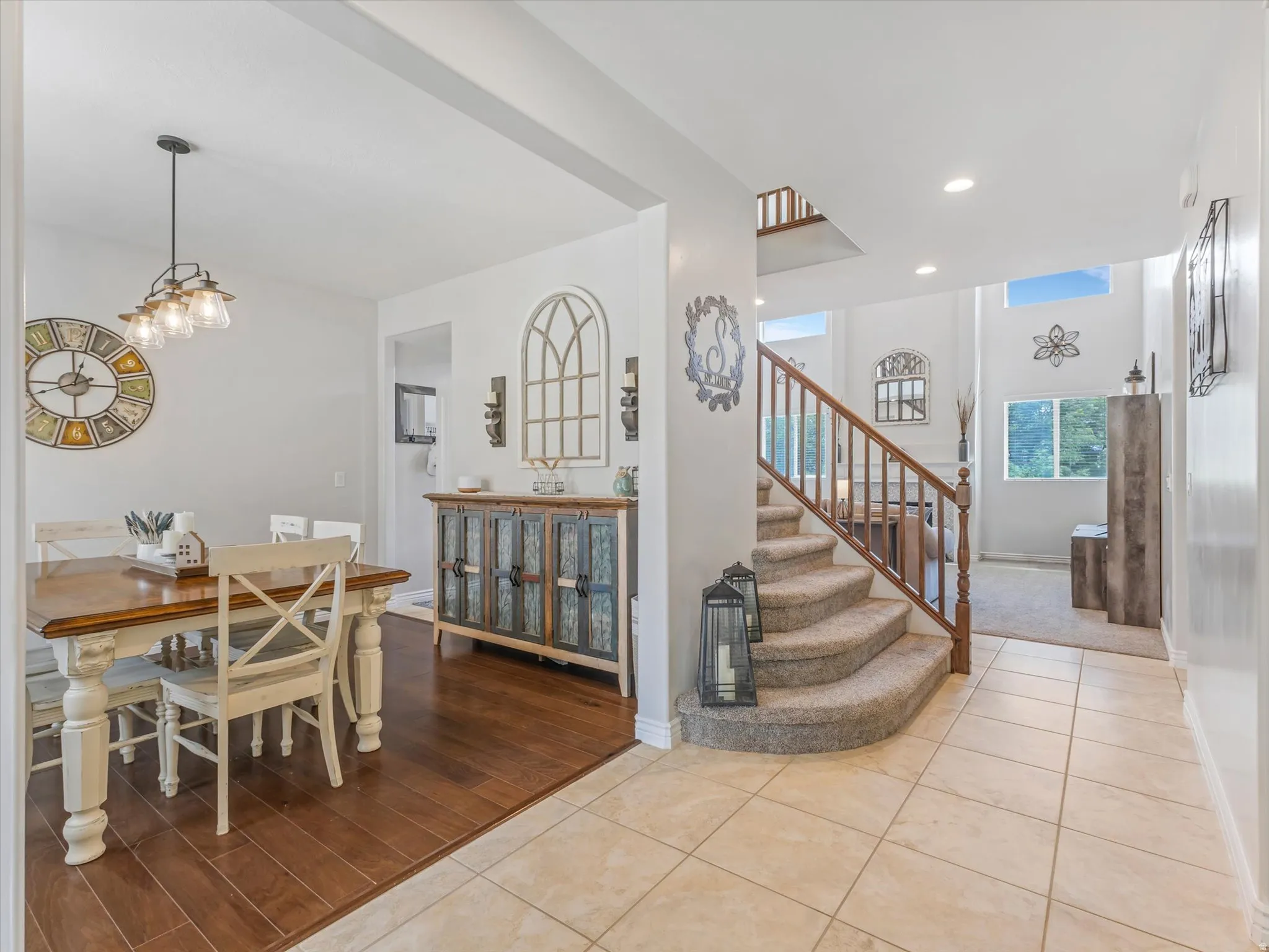 Two-story entryway with a carpeted staircase and wood railing, featuring neutral tile flooring