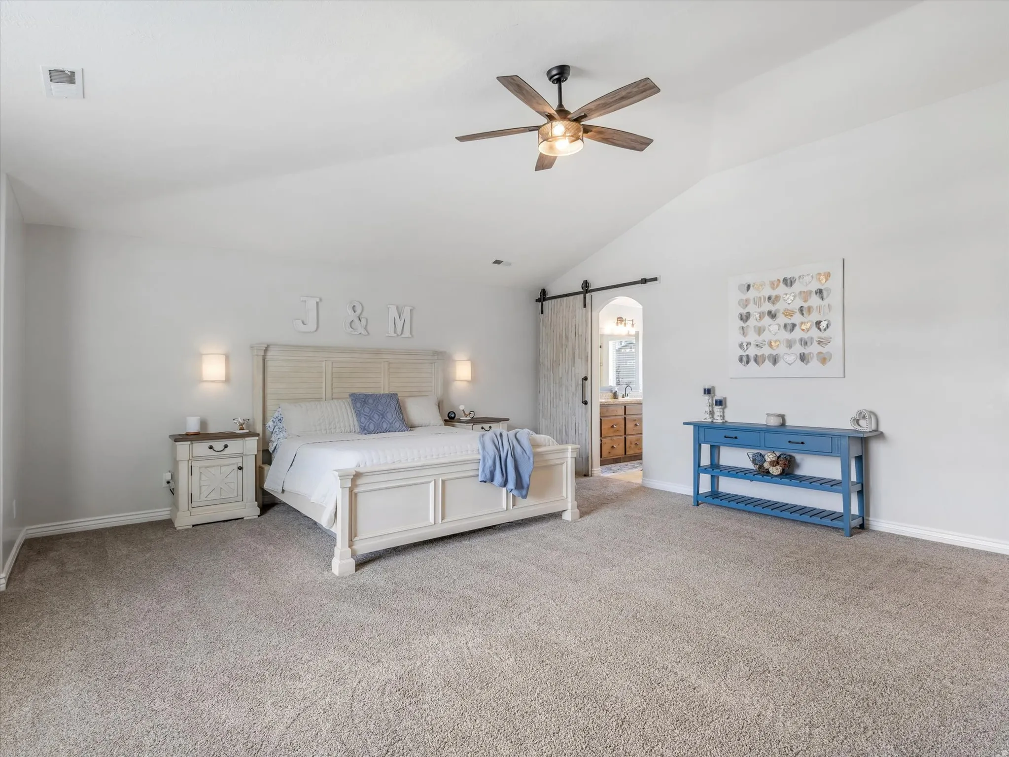 Spacious room featuring vaulted ceilings, a ceiling fan with light fixture, wall-mounted sconce lighting, and a barn door entry to an additional space