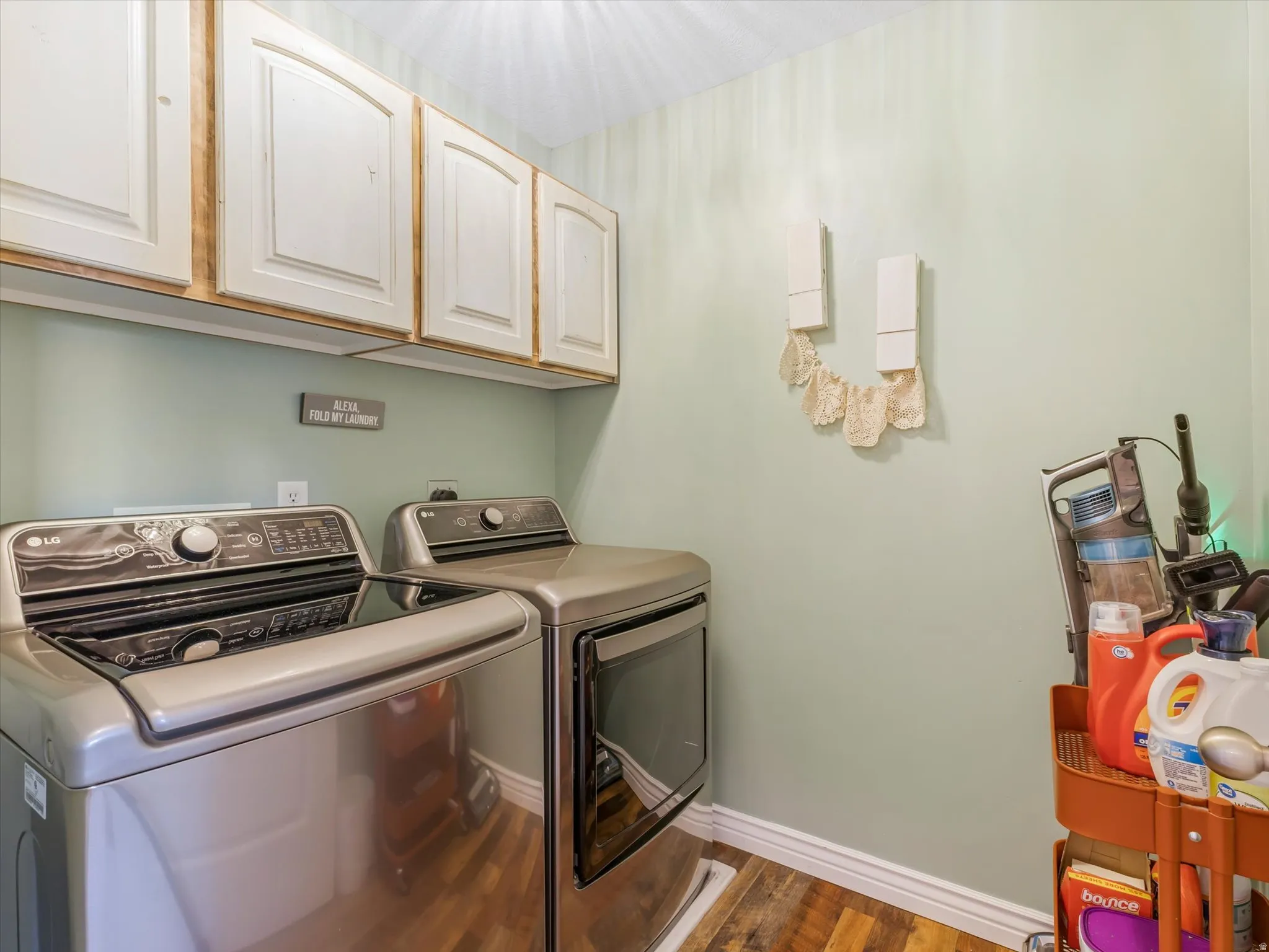 Wood-finish flooring anchors this space featuring white wall-mounted cabinetry, a light green wall finish, and white baseboards