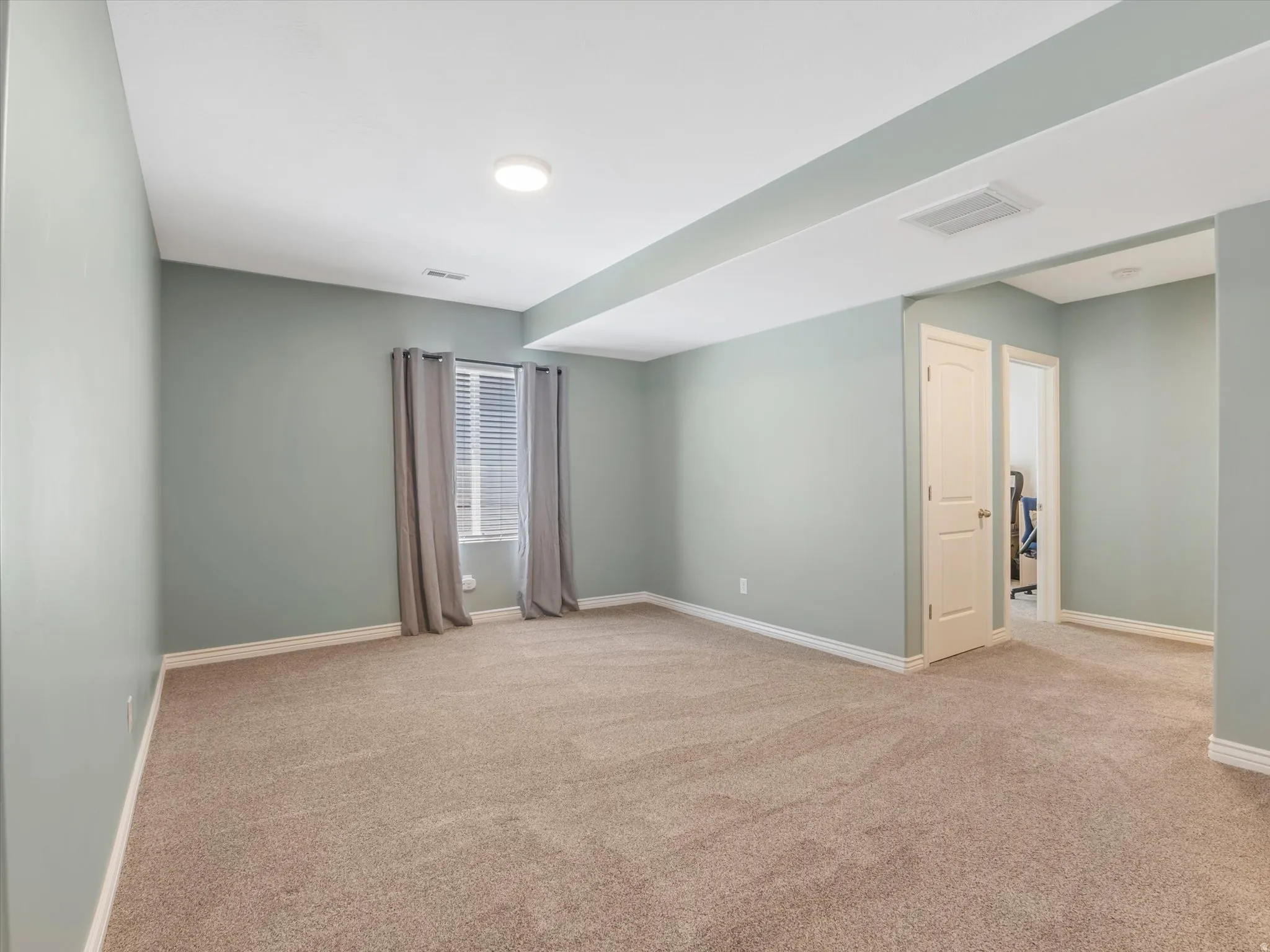 Spacious room featuring neutral-toned carpeting, light-colored walls, and a window with blinds