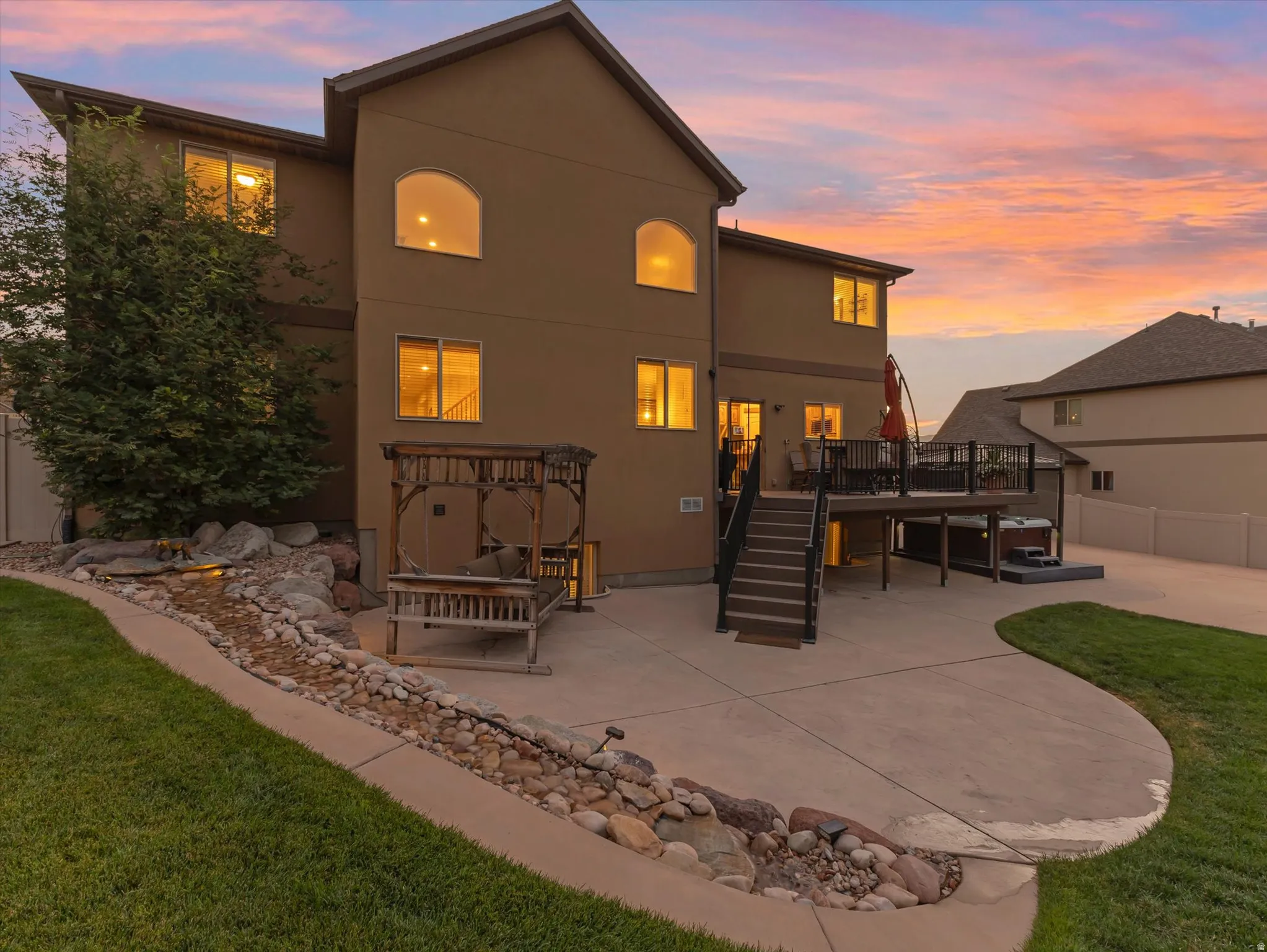 Rear exterior featuring a multi-level deck with black railings, a spa, and concrete patio