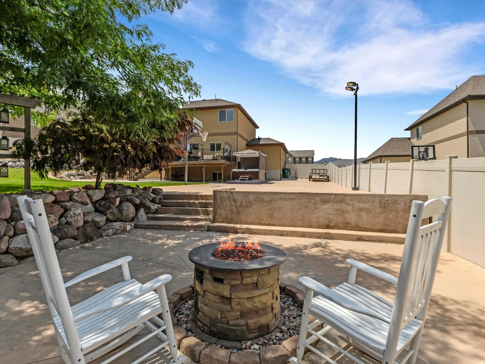 Expansive stamped concrete patio featuring a built-in stone fire pit, a tiered rock retaining wall, and defined concrete steps