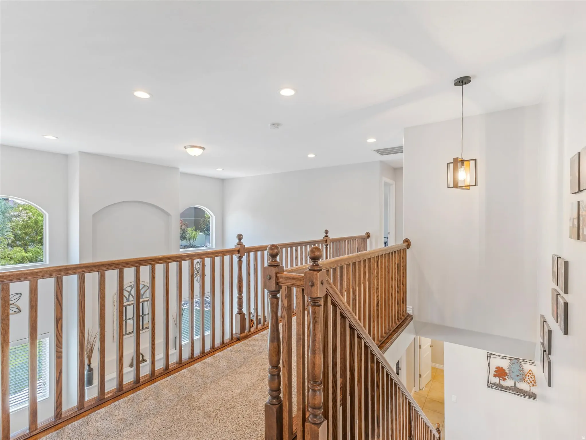 Upper-level hallway with wood-finish railings, recessed lighting, and a contemporary pendant fixture