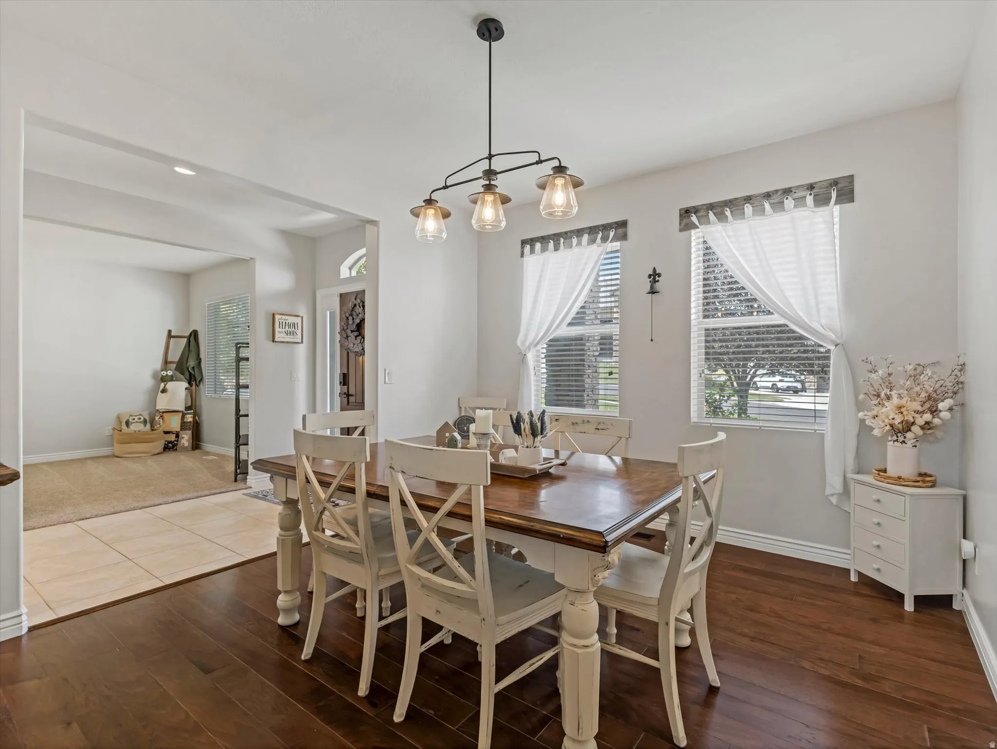 Dining area with rich wood-finish flooring, featuring a linear chandelier with three glass shades