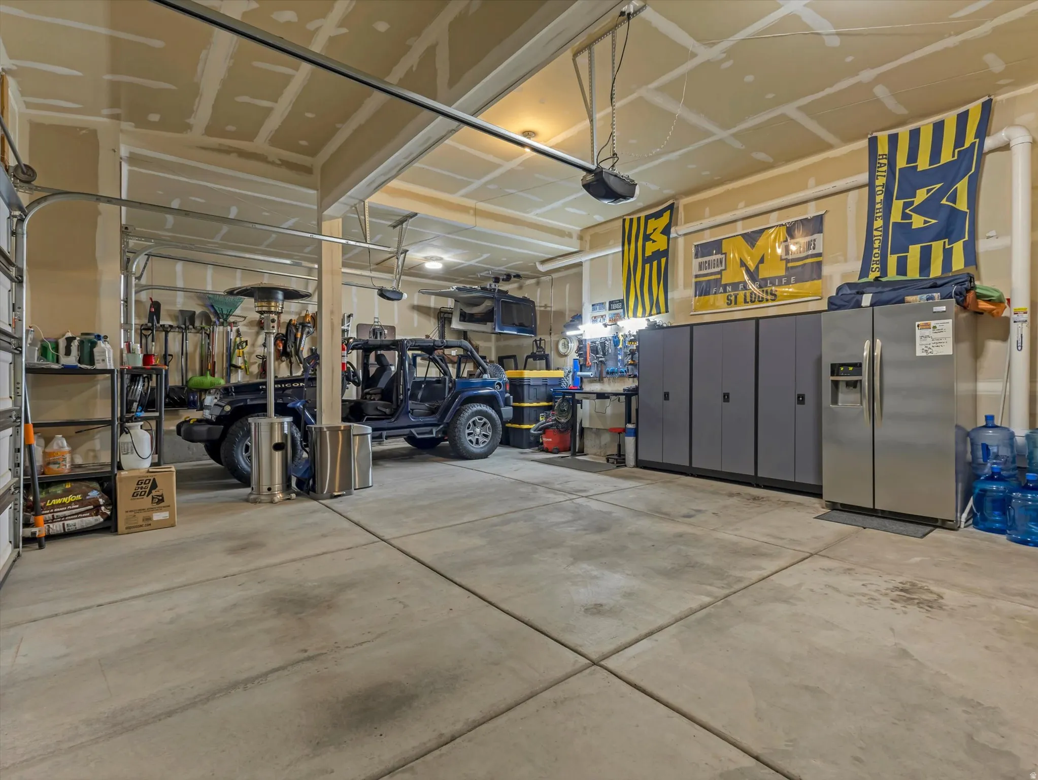 Spacious two-car garage featuring a concrete floor, built-in storage cabinets, and a side-by-side refrigerator