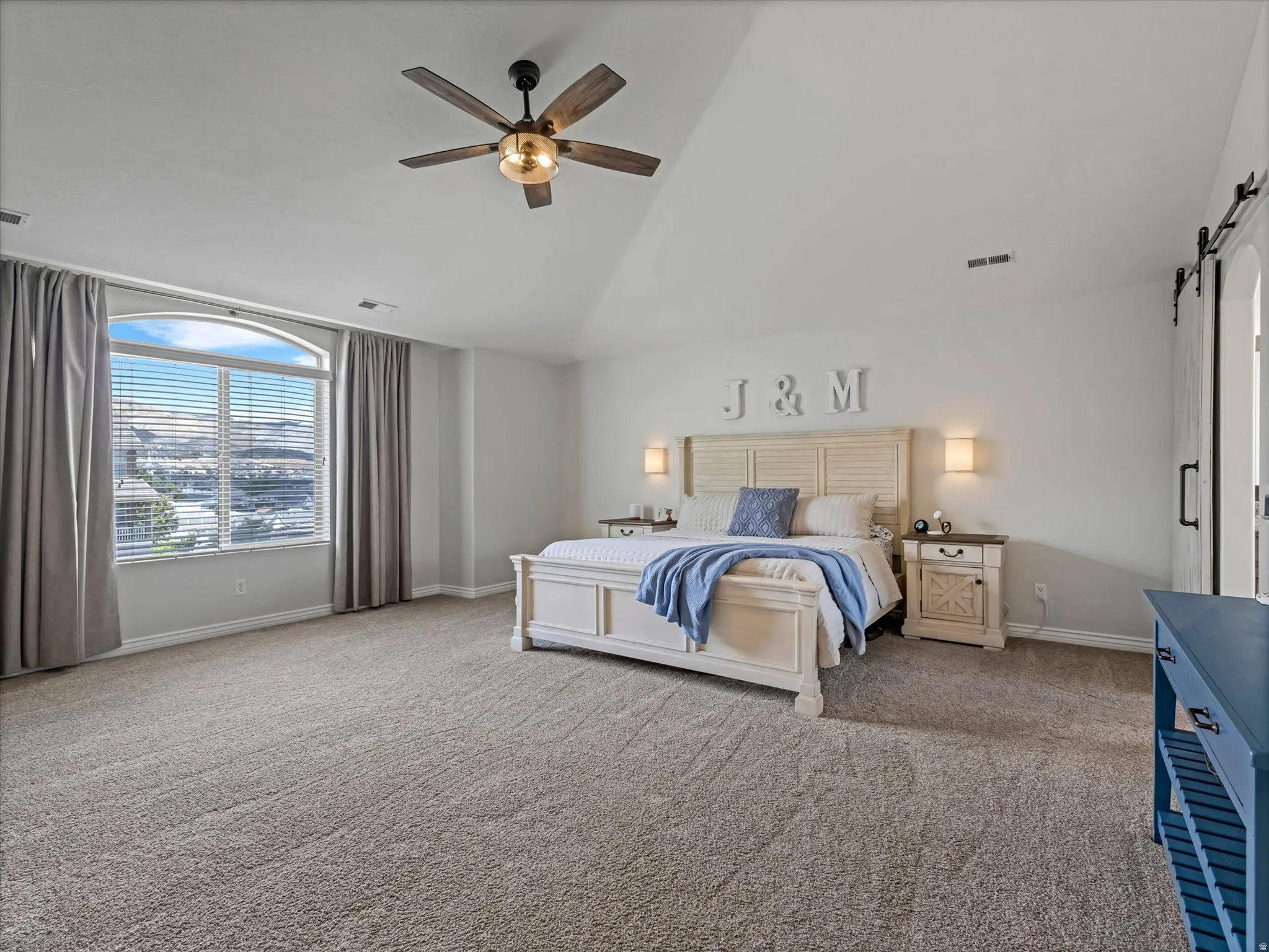 Spacious bedroom featuring vaulted ceilings, a large arched window with blinds, soft carpeting, and a ceiling fan with integrated lighting
