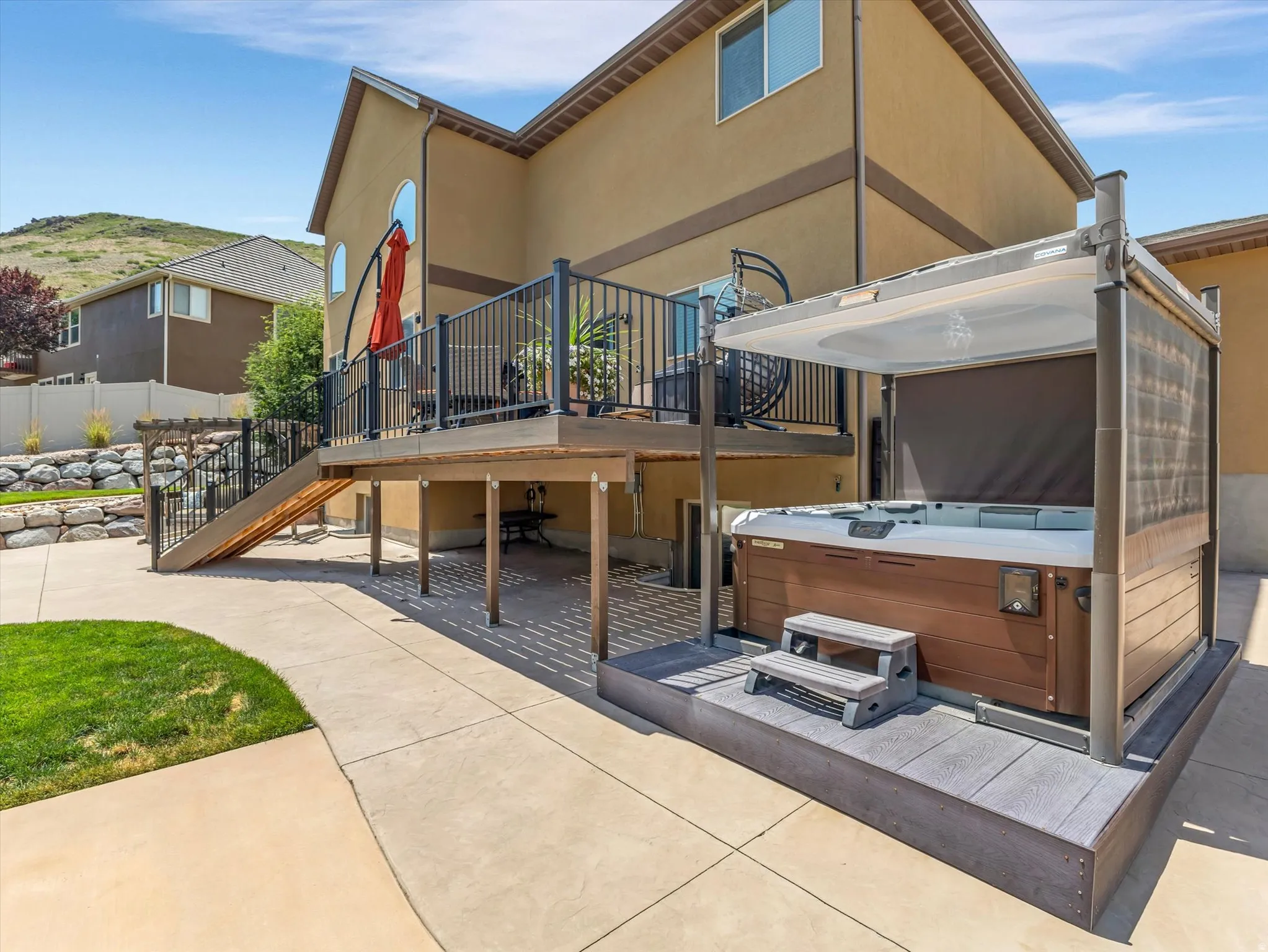Outdoor patio featuring a hot tub with a retractable canopy, a multi-level deck with black railings, a concrete patio, and a sloped retaining wall