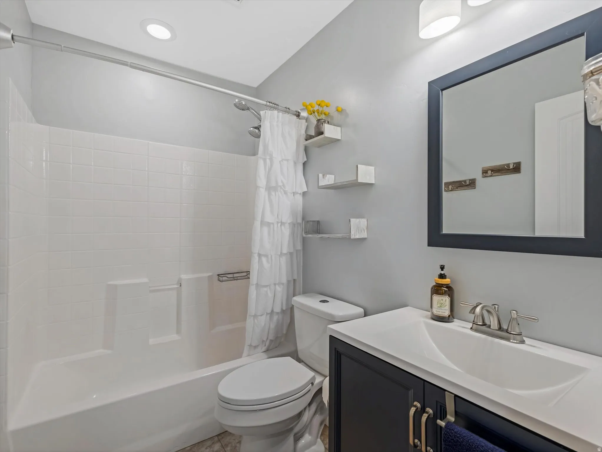 Full bathroom featuring a tub/shower combination with white tile surround, a built-in toilet, a dark vanity with a white countertop and integrated sink, and a framed mirror