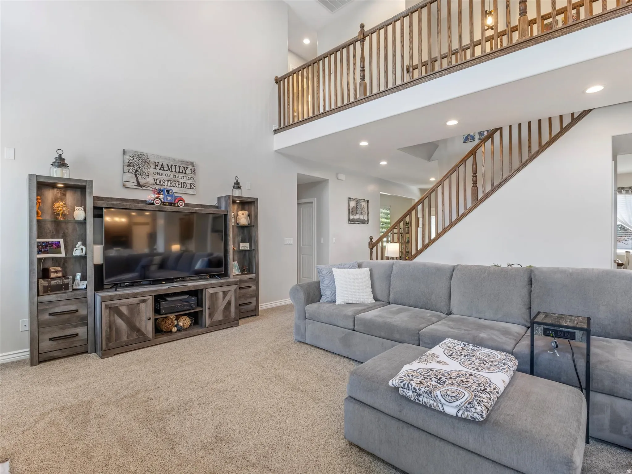 Spacious living area featuring a two-story ceiling, recessed lighting, carpet flooring, and a two-story staircase with wood balusters and handrails