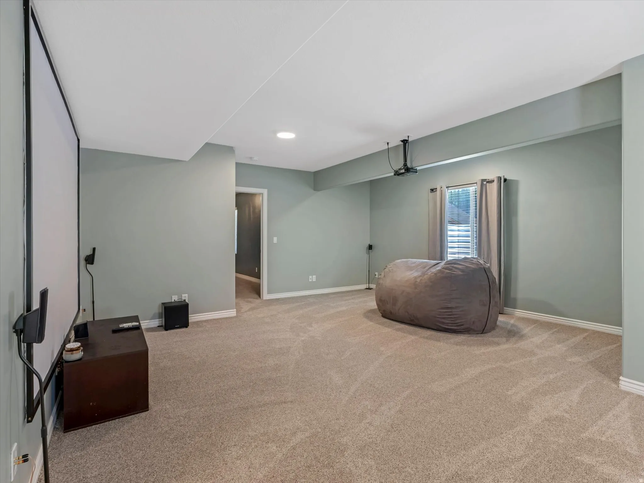 Spacious room featuring a large projector screen, recessed lighting, and neutral carpeting