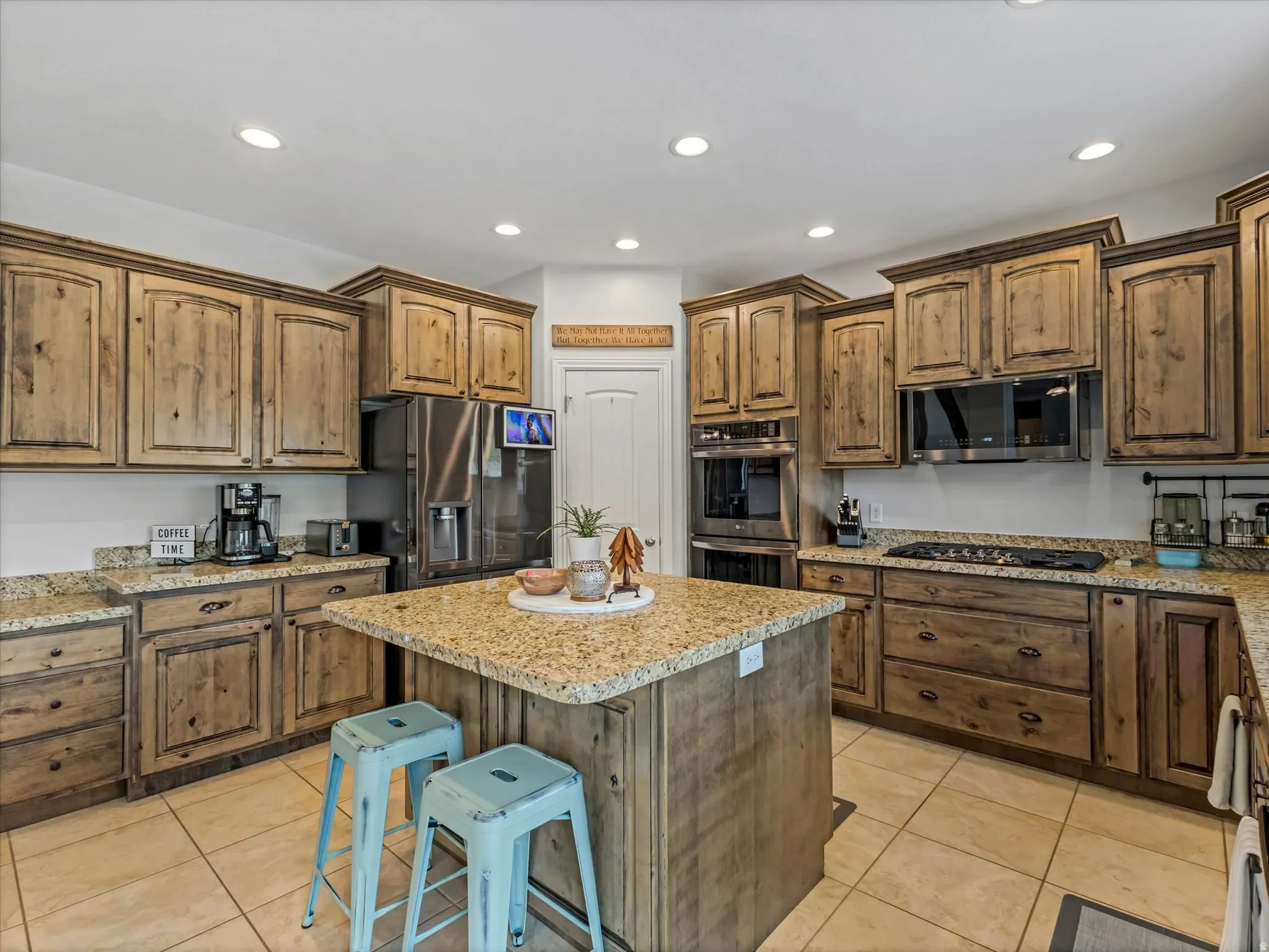Kitchen featuring extensive wood-finish cabinetry, a central island with a granite-style countertop, stainless steel appliances, recessed lighting, and tile flooring
