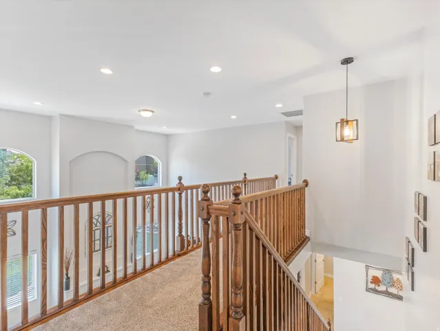 Upper-level hallway with wood-finish railings, recessed lighting, and a contemporary pendant fixture