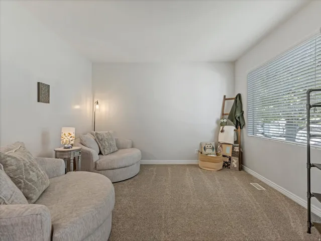Spacious room featuring neutral carpeting, light gray walls, a large window with horizontal blinds, and white baseboards