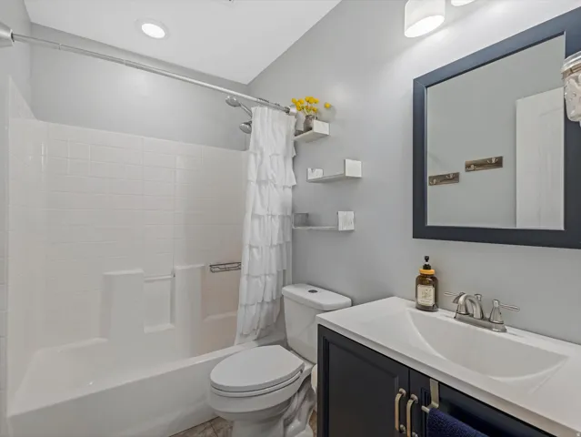 Full bathroom featuring a tub/shower combination with white tile surround, a built-in toilet, a dark vanity with a white countertop and integrated sink, and a framed mirror