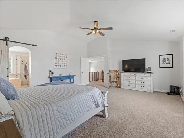 Spacious carpeted bedroom with vaulted ceilings and a ceiling fan