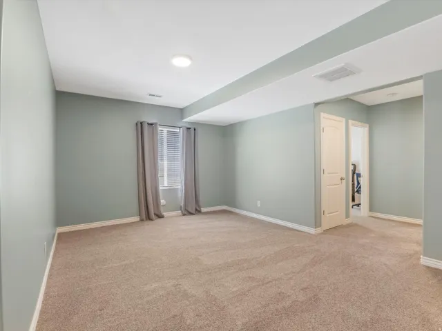 Spacious room featuring neutral-toned carpeting, light-colored walls, and a window with blinds