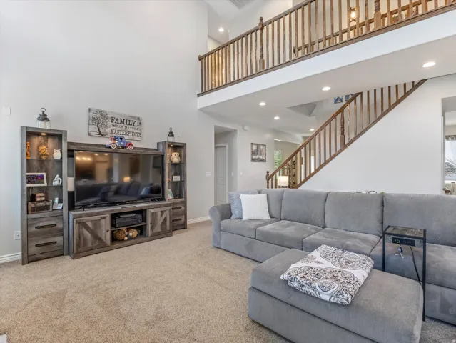 Spacious living area featuring a two-story ceiling, recessed lighting, carpet flooring, and a two-story staircase with wood balusters and handrails