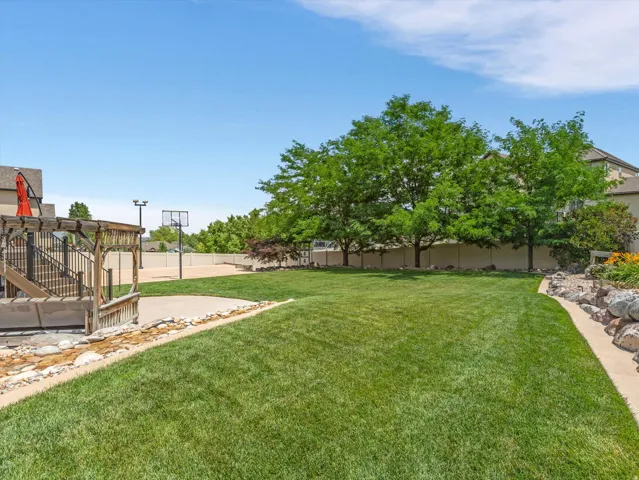 Expansive backyard featuring a manicured lawn, a wooden deck with a pergola, a hardscape patio, a basketball court, and mature trees