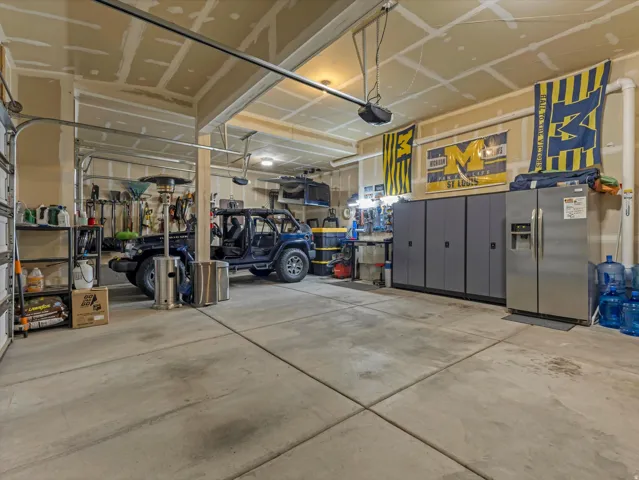 Spacious two-car garage featuring a concrete floor, built-in storage cabinets, and a side-by-side refrigerator