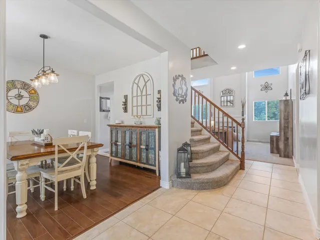 Two-story entryway with a carpeted staircase and wood railing, featuring neutral tile flooring