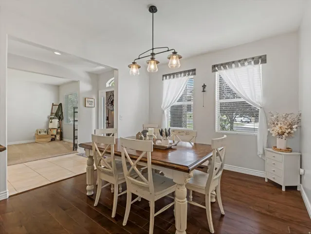 Dining area with rich wood-finish flooring, featuring a linear chandelier with three glass shades