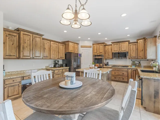 Expansive kitchen featuring light wood cabinetry, stone countertops, a central island, stainless steel appliances, and recessed lighting