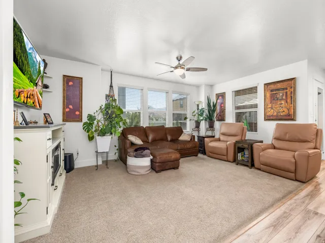 Carpeted living area featuring a ceiling fan, multiple windows with blinds, a built-in media console with storage, and an integrated electric fireplace