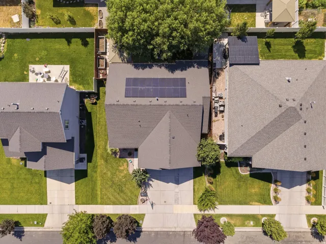 Residential property featuring a shingled roof with solar panels, a paved driveway, and a front yard with established landscaping