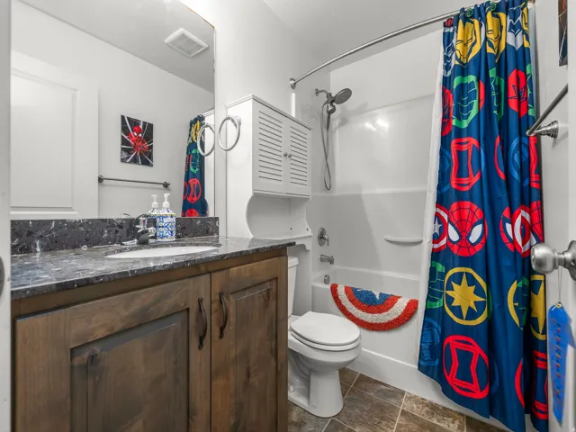 Bathroom featuring a dark wood-finish vanity with an undermount sink, a dark speckled countertop, and a white bathtub with an integrated shower