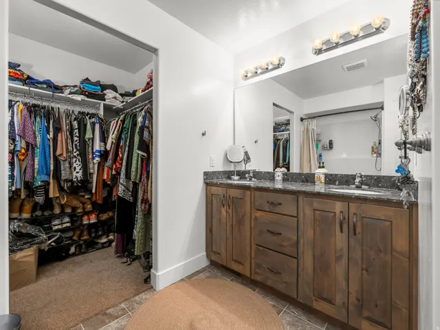 Bathroom featuring a dual-sink vanity with wood-finish cabinetry and a dark stone countertop