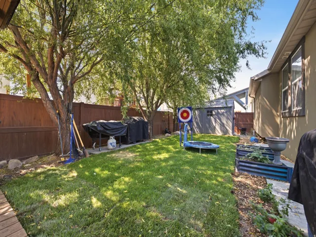 Private backyard featuring mature trees, a manicured lawn, a wood privacy fence, a storage shed, and raised garden beds