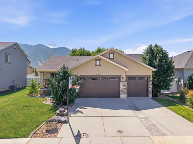 Exterior featuring a light tan stucco finish with stone accents, a two-car garage with carriage-style doors, a concrete driveway, and a manicured front lawn