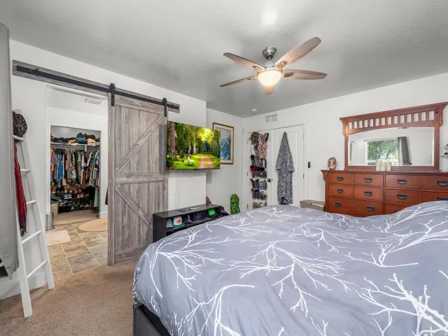 Bedroom featuring a wood-look barn door, ceiling fan with integrated lighting, and carpet flooring