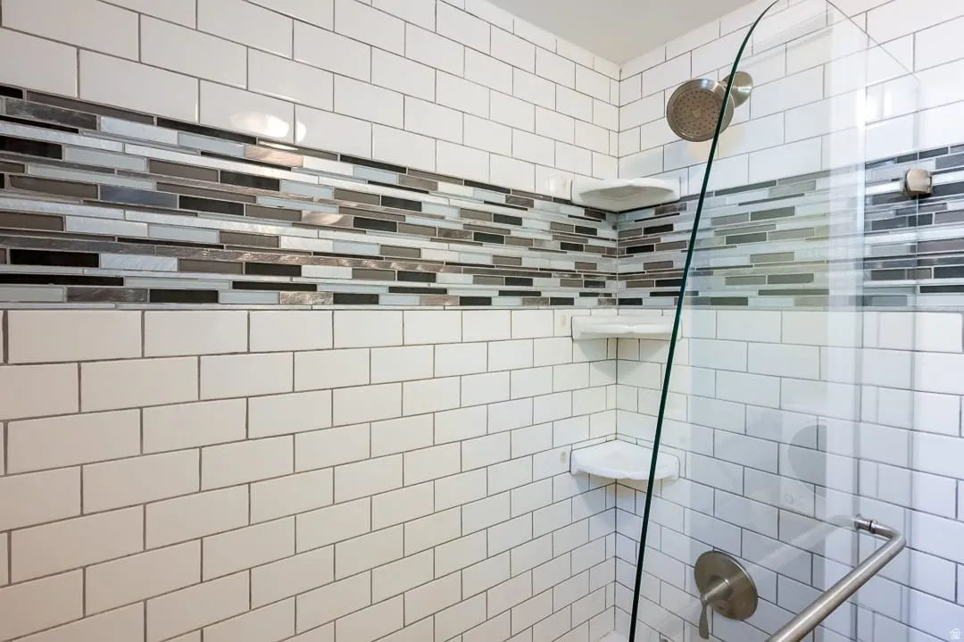 Shower enclosure featuring white subway tile, a decorative glass tile accent band, built-in corner shelves, a glass shower door, and brushed nickel fixtures
